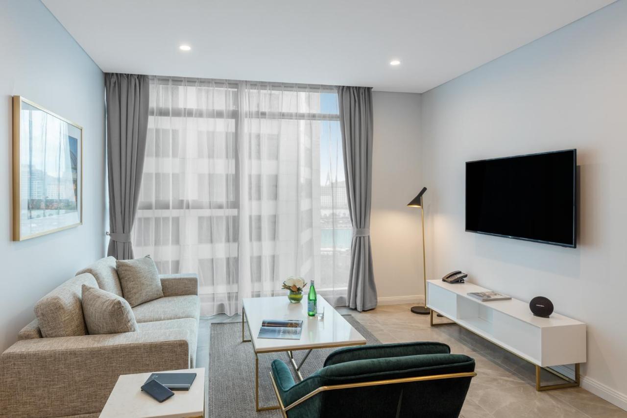 Meriton Suites Sussex Street, Sydney Kültér fotó The photo shows a modern living room space with a light, airy ambiance. It features a comfortable beige sofa with decorative cushions, a sleek coffee table placed in front, and a dark green armchair. There is a large window covered with sheer curtain