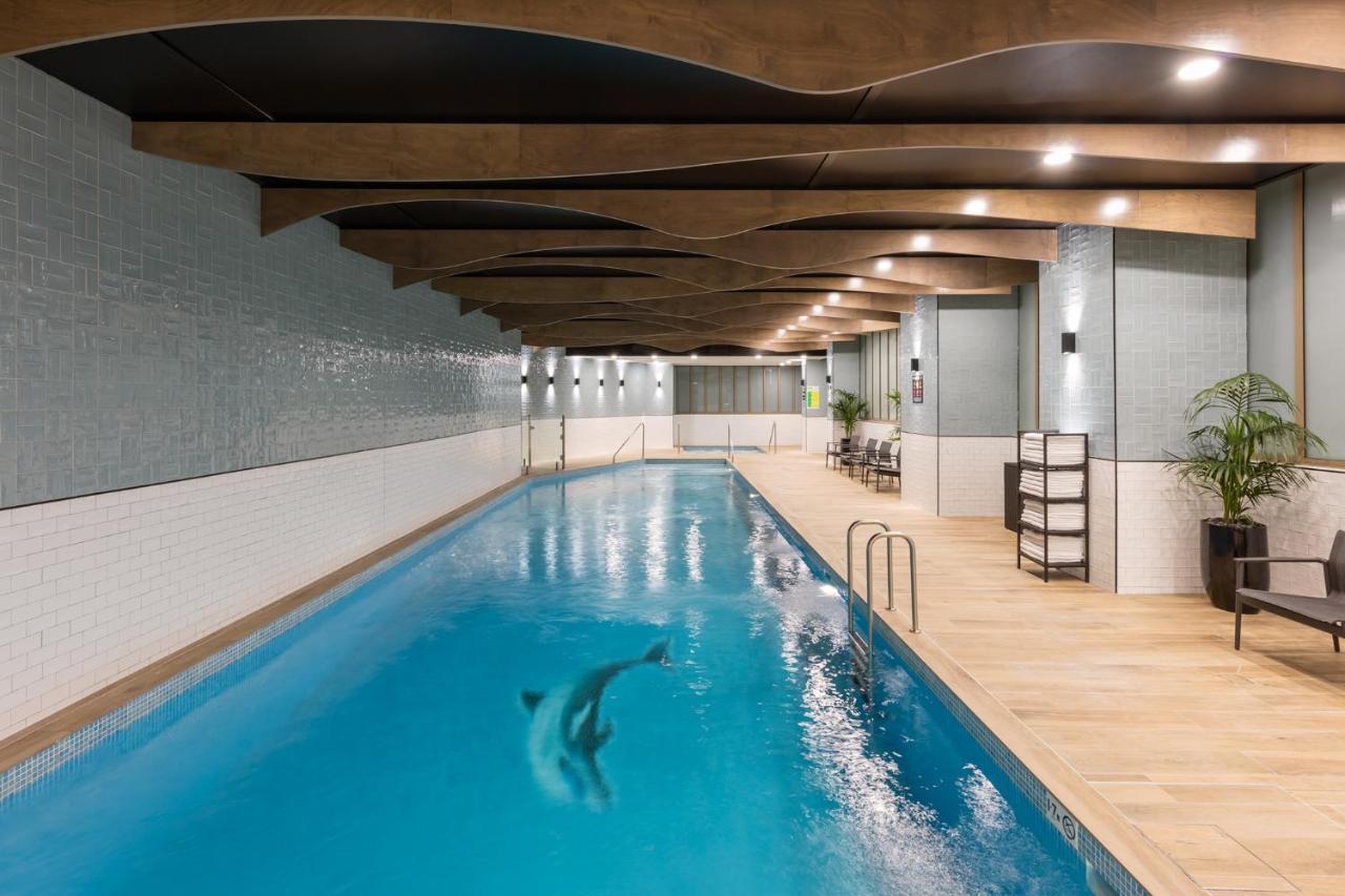 Meriton Suites Sussex Street, Sydney Kültér fotó The photo shows an indoor swimming pool. The pool features clear blue water, and there is a dolphin swimming in it. The surrounding area has a modern design with curved wooden beams on the ceiling, and the walls are tiled in light colors. There are a