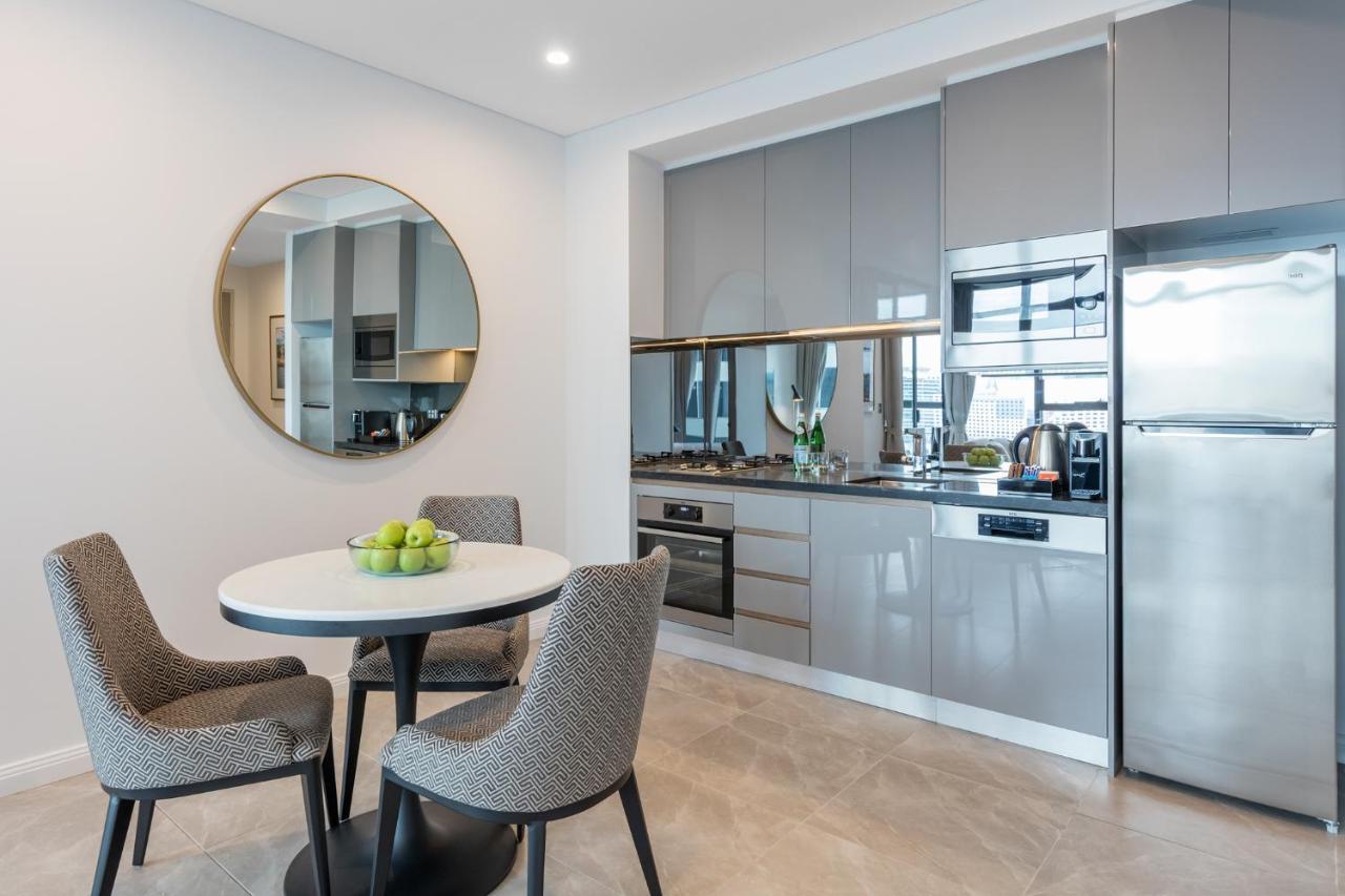 Meriton Suites Sussex Street, Sydney Kültér fotó The photo features a modern kitchen and dining area. The kitchen has sleek grey cabinets and countertops, with built-in appliances including an oven and possibly a cooktop. There's a large stainless steel refrigerator on the right. A round dining tab