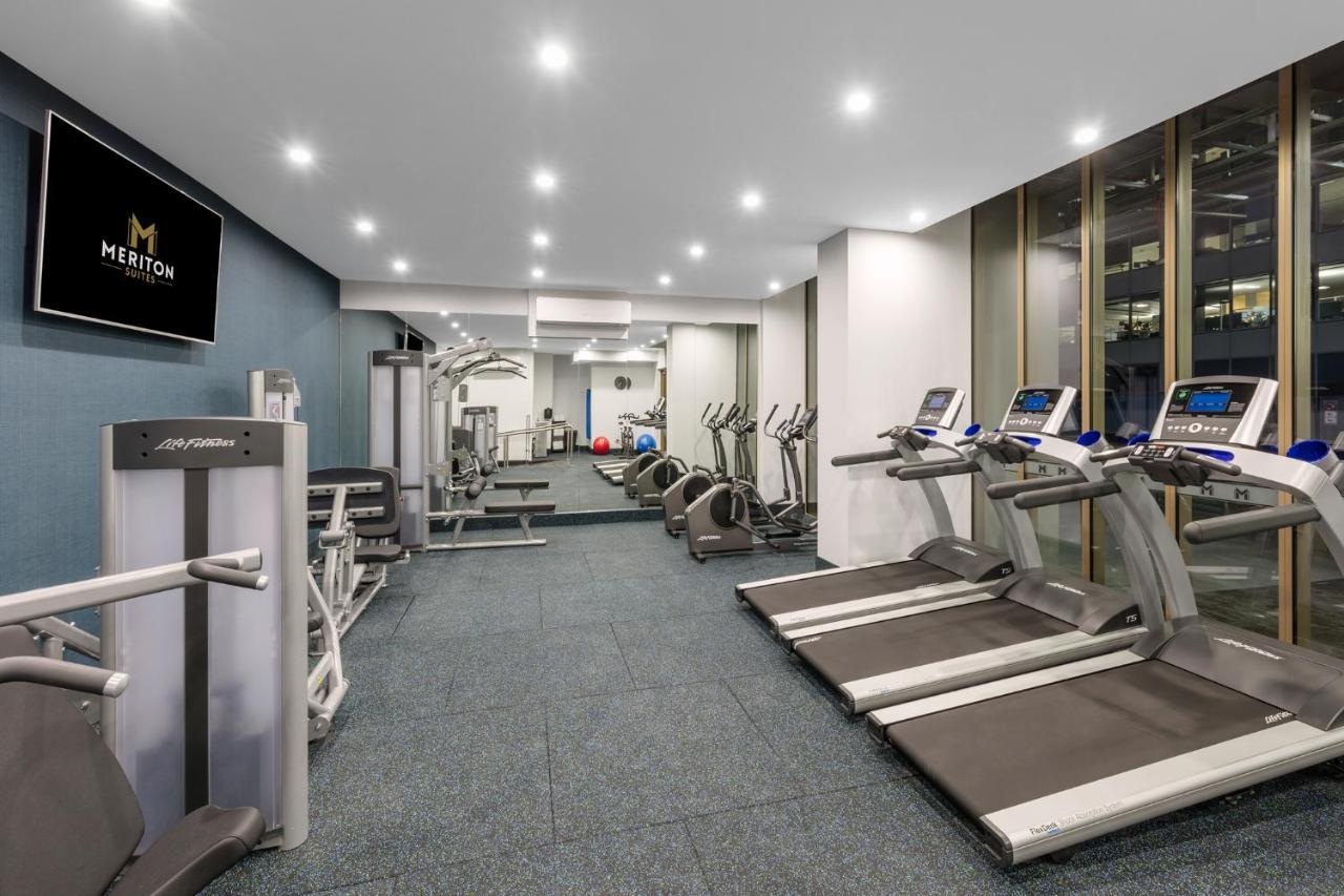 Meriton Suites Sussex Street, Sydney Kültér fotó The photo shows a modern gym space. It features various exercise equipment, including several treadmills and elliptical machines positioned along one side. On the other side, there are weight machines and additional fitness equipment. The gym has a c