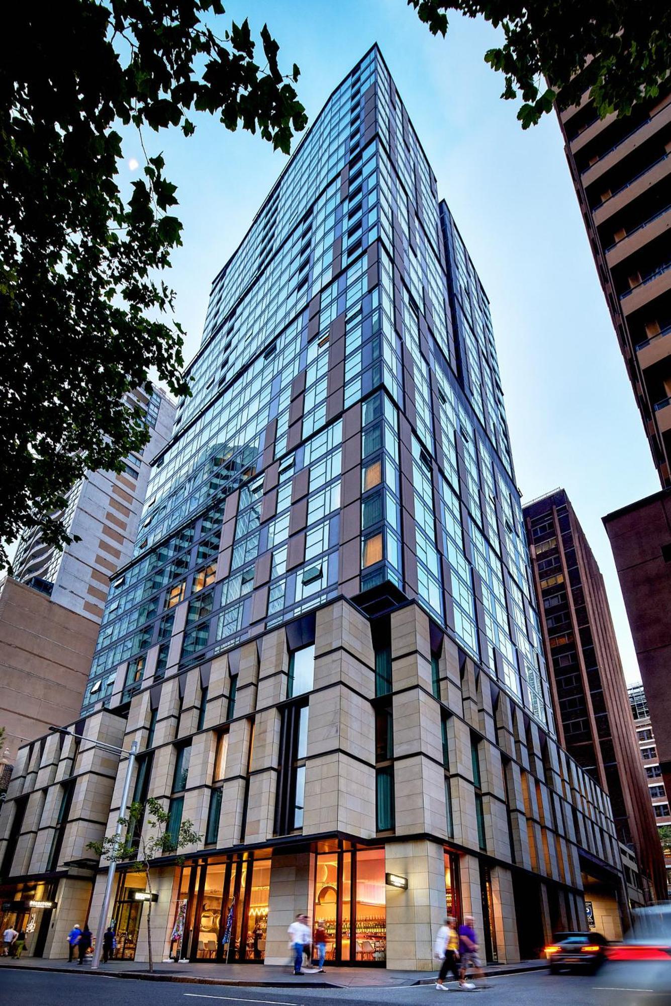Meriton Suites Sussex Street, Sydney Kültér fotó The photo shows a modern high-rise building with a sleek, glass facade reflecting its surroundings. The structure features a combination of glass and concrete materials, with multiple stories visible. The lower part of the building has a sturdy, text